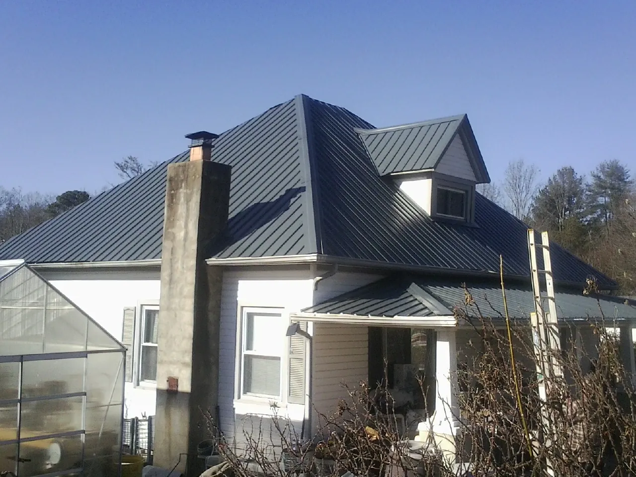 Dark blue standing seam metal roof on a white farmhouse with dormer — Slate & Tile Roof Repair by Roofing Brothers in Wanette
