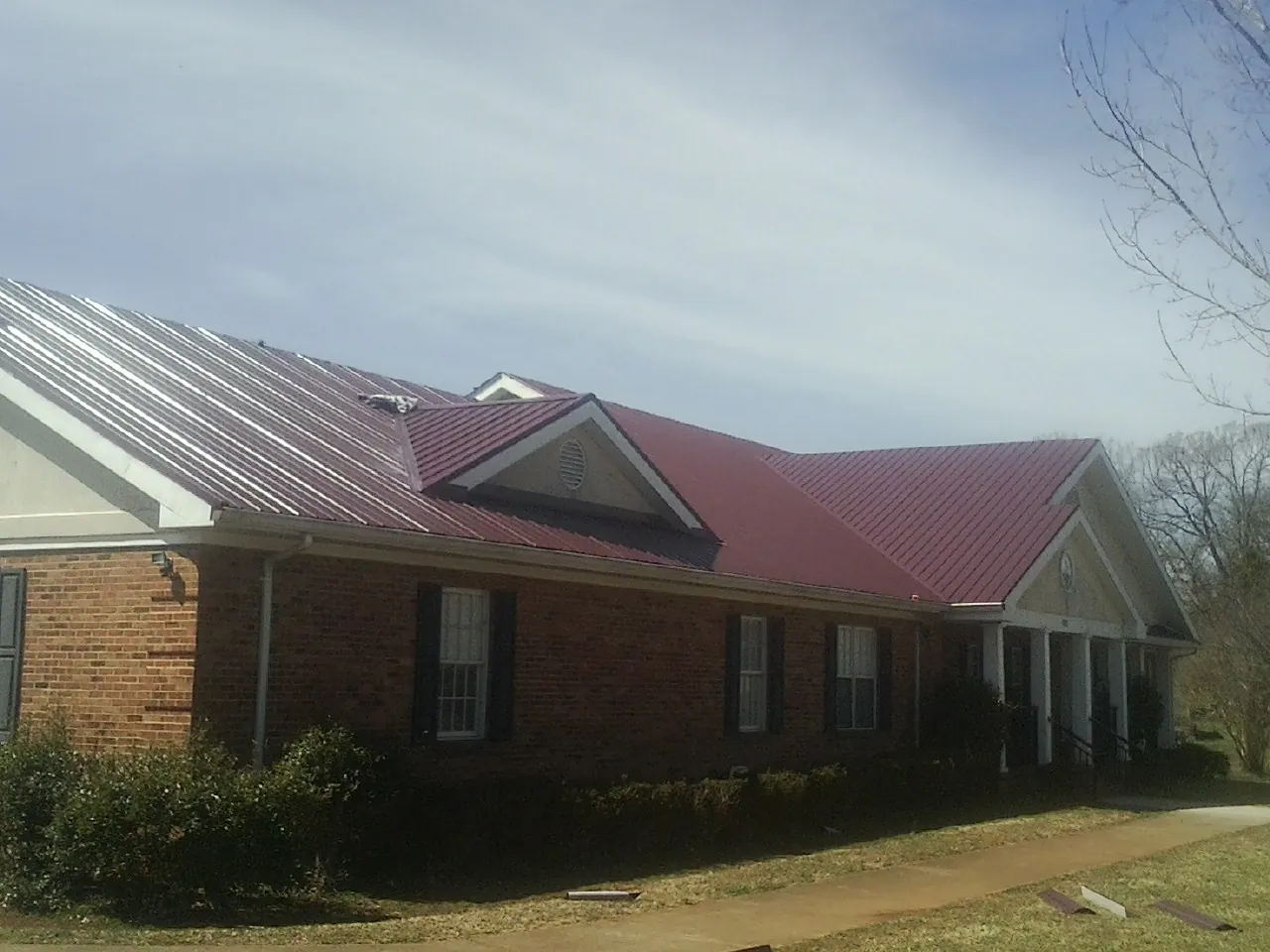 Red metal roof with gabled entries on a long brick building, from a Hail Damage Roof Repair job in Wanette