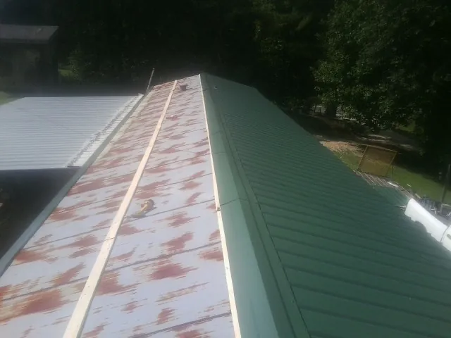 Old rusted panels beside newly installed green metal roofing — Wind Damage Roof Repair by Roofing Brothers in Wanette