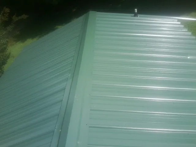 New green metal panels meeting at the ridge of a roof — Flat Roof Repair work by our crew in Wanette