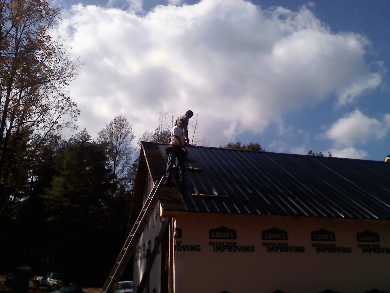 Roofer fastening dark metal panels high against a cloudy sky, from a Roof Inspection job in Wanette