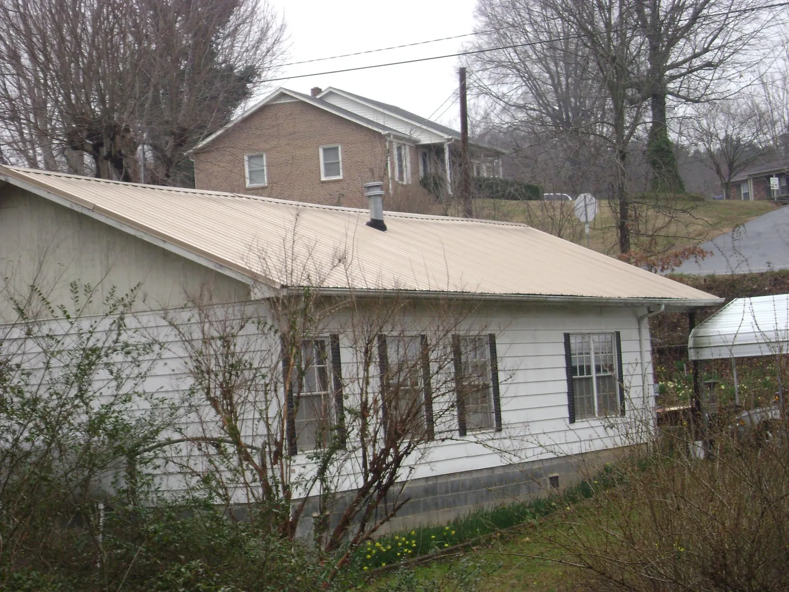 Tan metal roof on a white sided house set into a hillside — Commercial Roofing by Roofing Brothers in Wanette