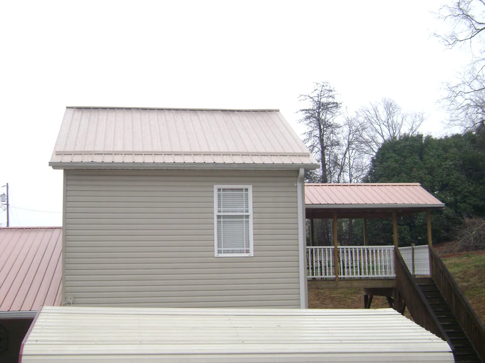 Tan metal roofs on a two story addition and attached porch, from a Roof Replacement job in Wanette